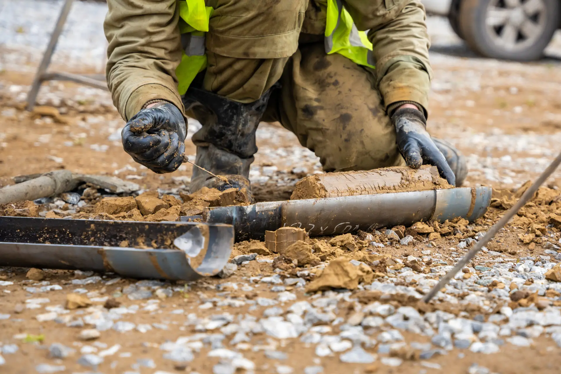 Drummond Carpenter nuclear solutions multidisciplinary coordination approach illustrated by a field technician in high-visibility gear and protective gloves carefully examining labeled soil core samples extracted from a borehole during a geotechnical and environmental site investigation, representing the firm's multidisciplinary expertise in subsurface characterization, radiological soil sampling, contaminated site assessment, and coordinated nuclear site investigation services.