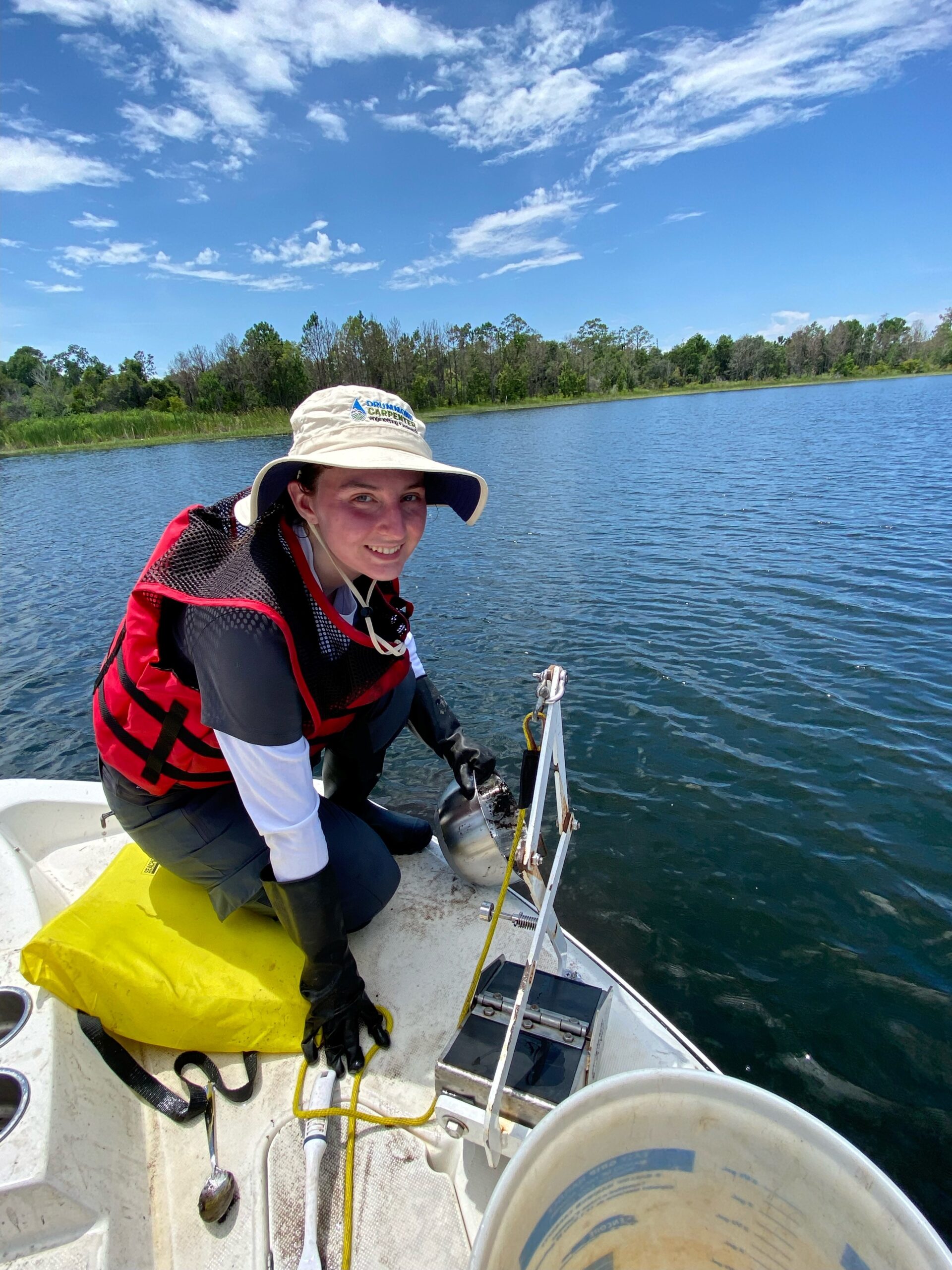 Drummond Carpenter environmental scientist collecting a sediment sample from a boat on a lake, using a grab sampler and a stainless steel sampling bowl.