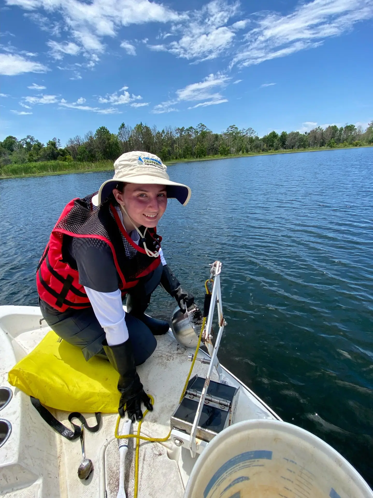 Drummond Carpenter environmental scientist collecting a sediment sample from a boat on a lake, using a grab sampler and a stainless steel sampling bowl.
