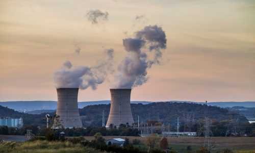 Drummond Carpenter nuclear solutions hero image featuring two large nuclear power plant cooling towers emitting steam at dusk against a golden sky, with high-voltage transmission lines and rural landscape in the foreground, representing the firm's expertise in nuclear facility engineering, radiological site assessment, nuclear infrastructure support, and Department of Energy project services.