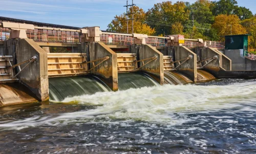 Drummond Carpenter water solutions approach to long-term performance illustrated by a multi-gate concrete dam and hydraulic control structure with active water flow, representing the firm's expertise in water control infrastructure, dam engineering, flood management, and resilient water systems design built for lasting performance.