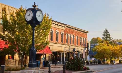 Historic Ypsilanti Michigan downtown infrastructure featuring a decorative cast iron street clock, brick streetscape, tree-lined sidewalks, and the restored Oliver House building with local small businesses.